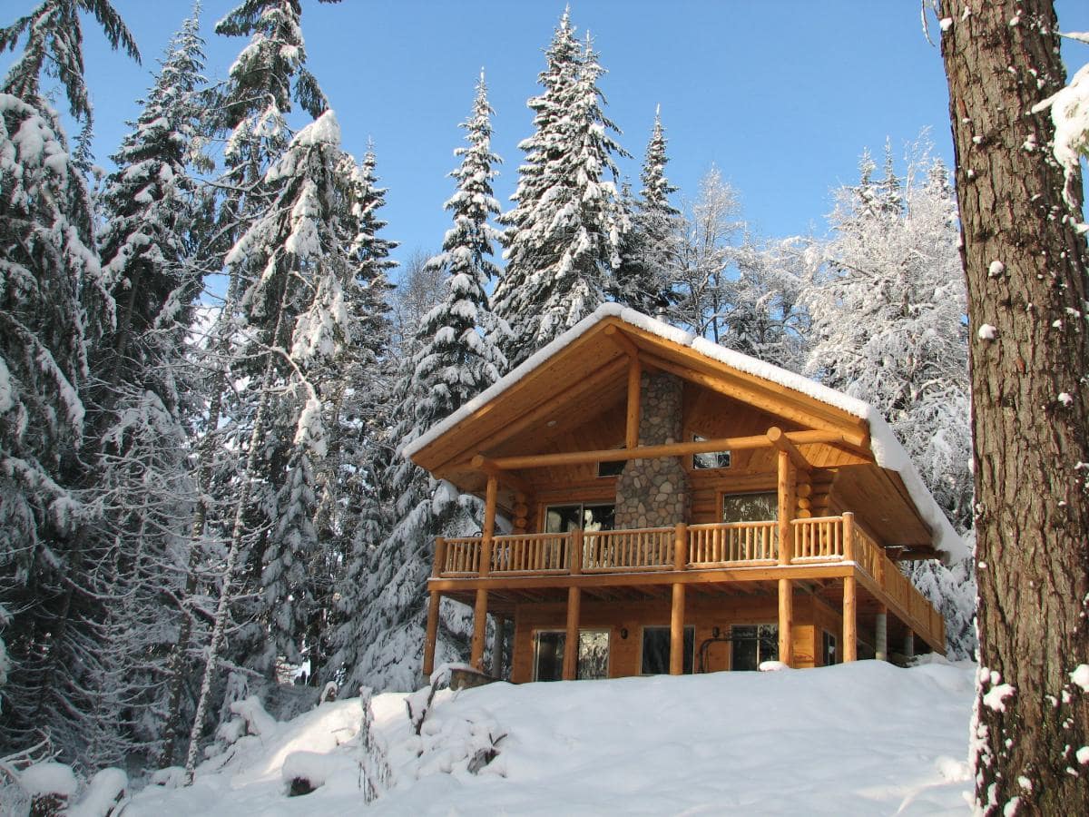 two story log cabin called the Meadow View Cabin sitting on a snowy hill in the forest at Western Pleasure Guest Ranch