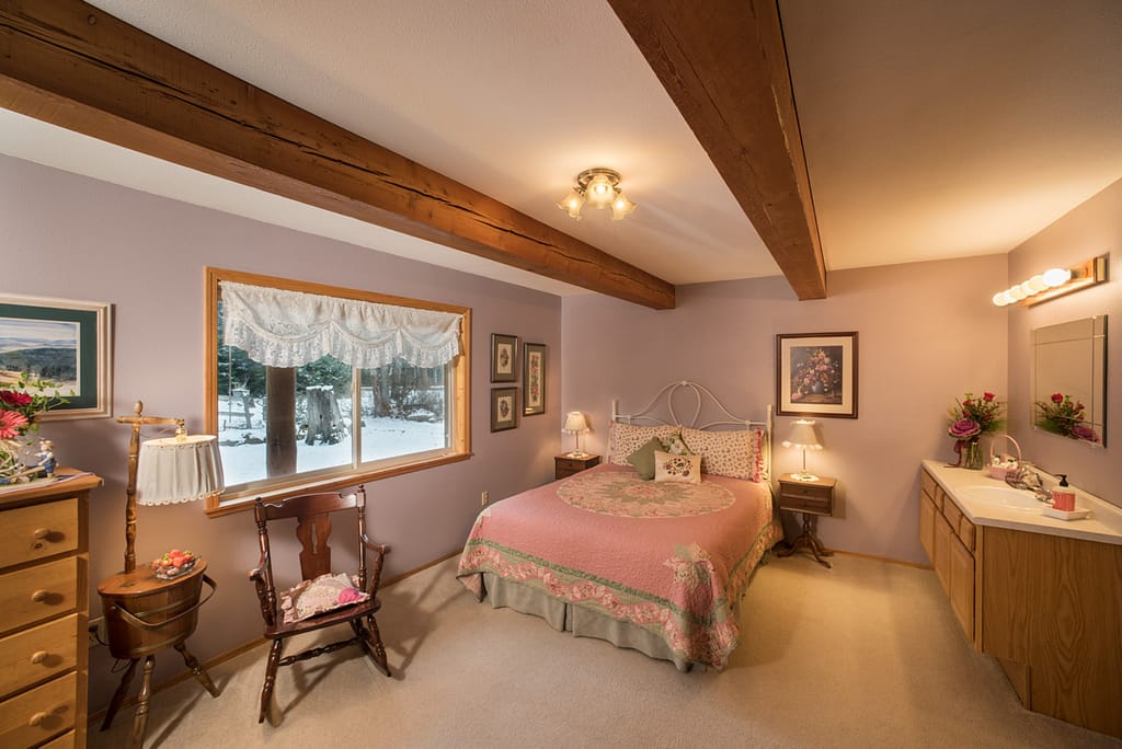 Guest room with quilted bed, rocking chair, bathroom vanity, and snow outside window