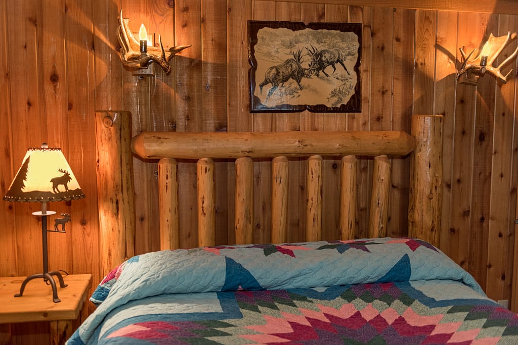 log bed with quilt in wood panel room with antler lights on the wall