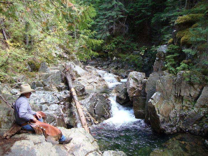 Cowboy sitting on rocks looking our at a small waterfall