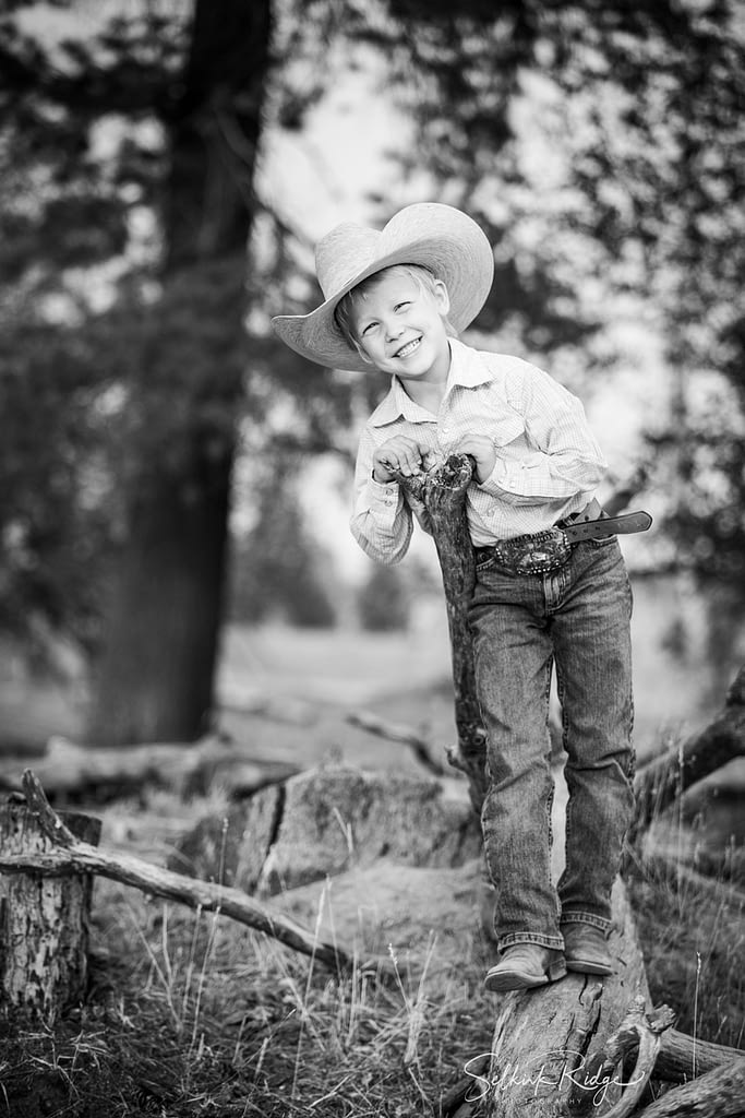 Little boy in cowboy hat leaning on a stick and smiling
