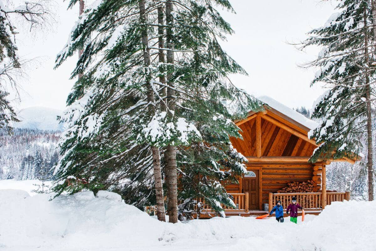 log cabin in the snow with children in front pulling sleds