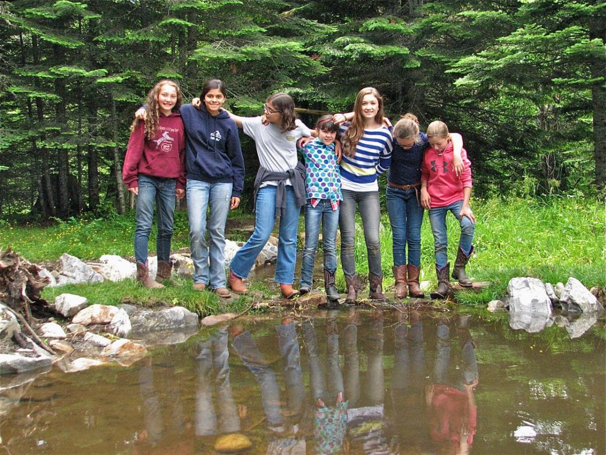 children standing in line with arms around each other next to a pond