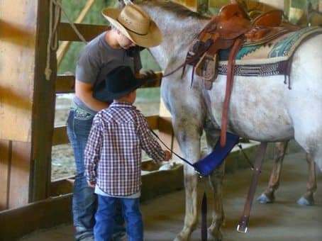 cowgirl teaching child how to saddle a horse at Western Pleasure Guest Ranch Youth Horsemanship Program