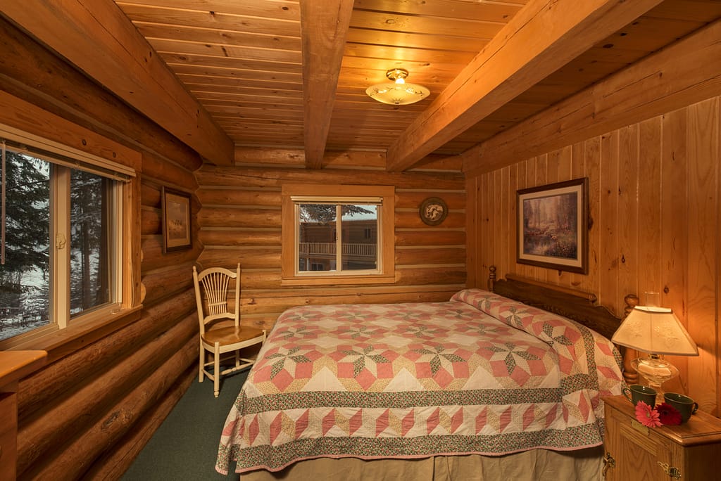Private bedroom in log cabin with quilted bed coffee cups on side table