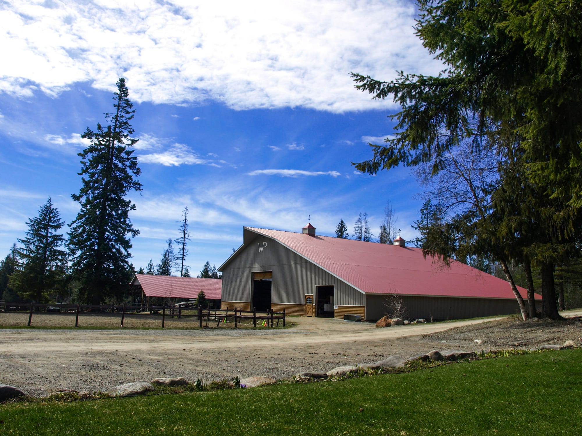 Large grey indoor arena barn with red roof and blue sky above
