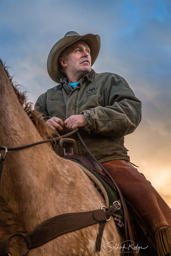 Cowboy ina green coat sitting on a horse tan horse