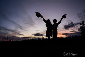 Silhouette of cowboy and cowgirl holding their hats up in the air